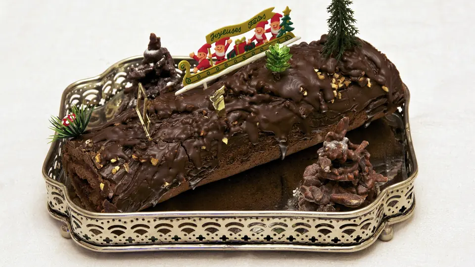 Schokoladen-Weihnachtsstamm mit Zuckerguss-Schild und Tannenzweigen auf einer silbernen Servierplatte